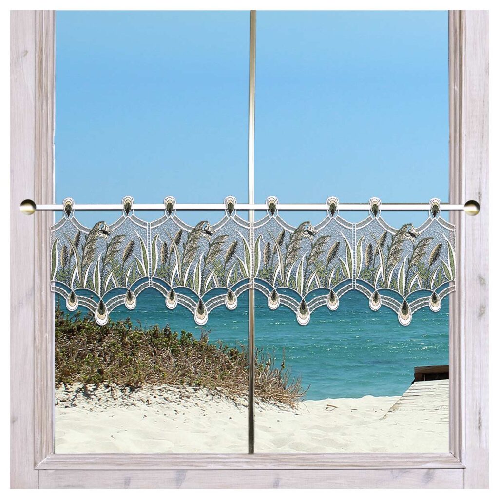 Ein Blick auf den Strand durch ein Fenster mit weiß gerahmten Scheiben. Der Vorhang weist ein kompliziertes Muster mit einem luftigen, gewellten Design und floralen Akzenten am oberen Rand auf. Im Hintergrund sind blaue Meereswellen und ein Sandstrand mit Vegetation zu sehen.